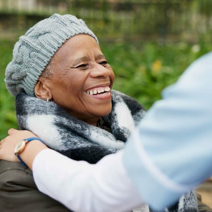 Baxter Senior Living | Nurse, smile and park with old woman in a wheelchair for retirement, elderly care and physical therapy. Trust, medical and healthcare with african patient and caregiver in nature for rehabilitation