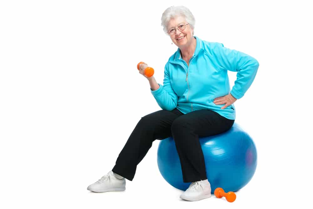 Senior woman sitting on an exercise ball flexing a small dumbbell