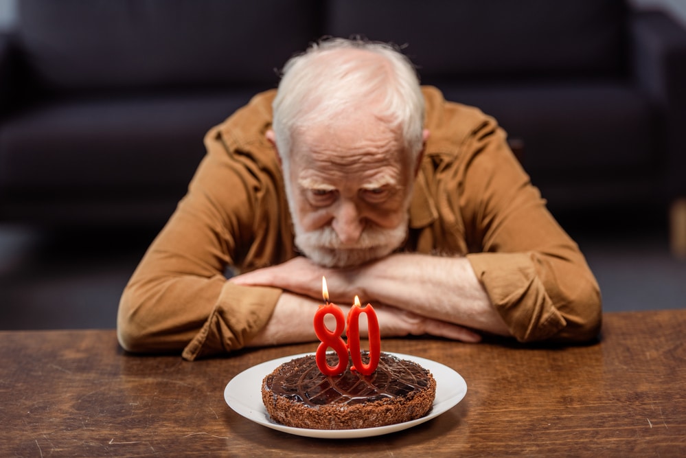 Senior man sitting in front of 80 yr old birthday cake looking depressed. Social Isolation and Dementia